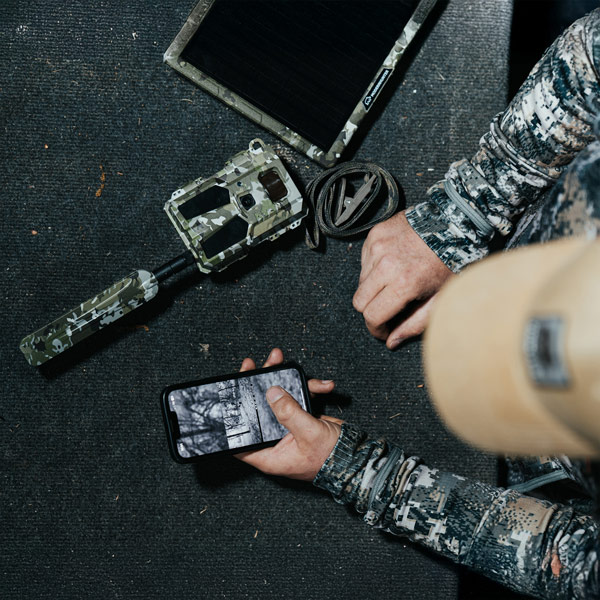 Das Bildmaterial der Bresser Modern Hunter Mini Wildkamera Hunter 4G wird vom Jäger auf dem Handy ausgelesen und angeschaut, das Bild zeigt außerdem die Wildkamera und ein Tablet